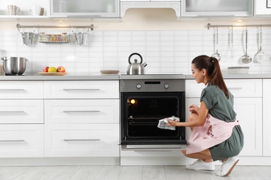 Photo of Young woman baking something in oven at home