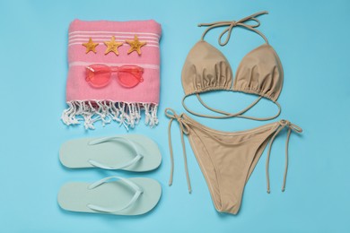 Stylish bikini and beach accessories on light blue background, flat lay. Space for text