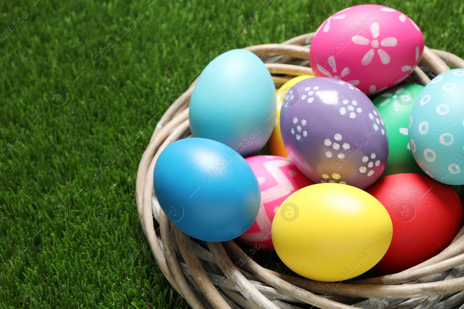 Photo of Colorful Easter eggs in decorative nest on green grass, closeup