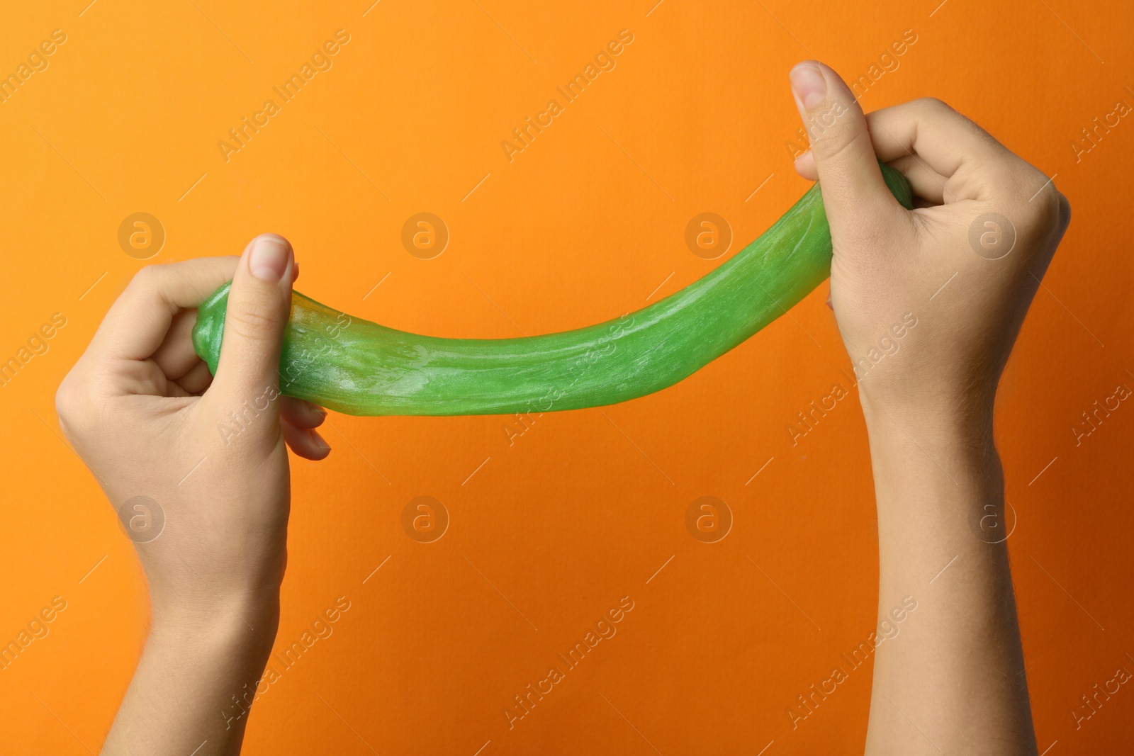 Photo of Woman playing with green slime on orange background, closeup. Antistress toy