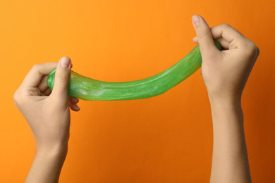 Woman playing with green slime on orange background, closeup. Antistress toy