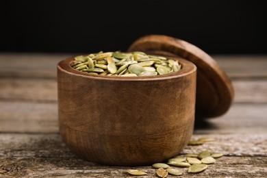 Photo of Dish with pumpkin seeds and lid on wooden table, closeup
