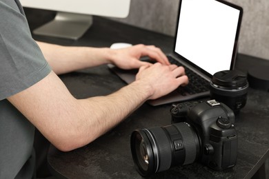 Photographer using laptop at dark table with camera, closeup