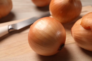 Photo of Many ripe onions and knife on wooden table, closeup