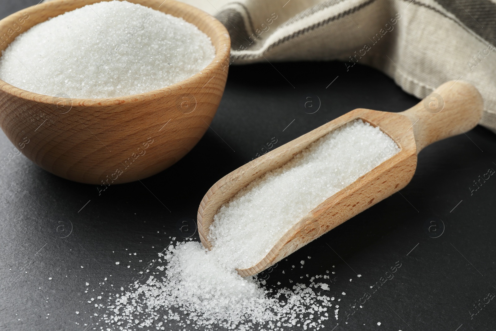 Photo of Granulated sugar in bowl and scoop on black table