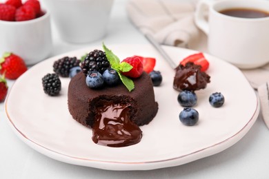 Photo of Plate with delicious chocolate fondant, berries and mint on white table, closeup