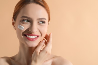 Beautiful young woman with sun protection cream on her face against beige background, space for text