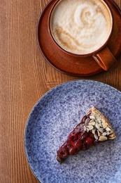 Cup of coffee and slice of cherry cake on wooden table, top view