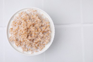 Tasty wheat porridge with milk in bowl on white table, top view. Space for text