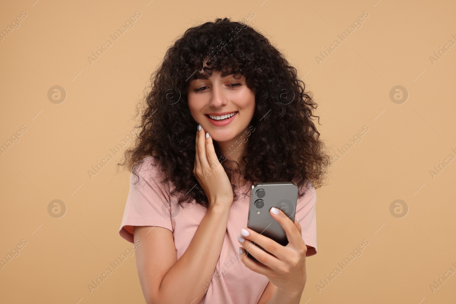 Photo of Happy young woman looking at smartphone on beige background