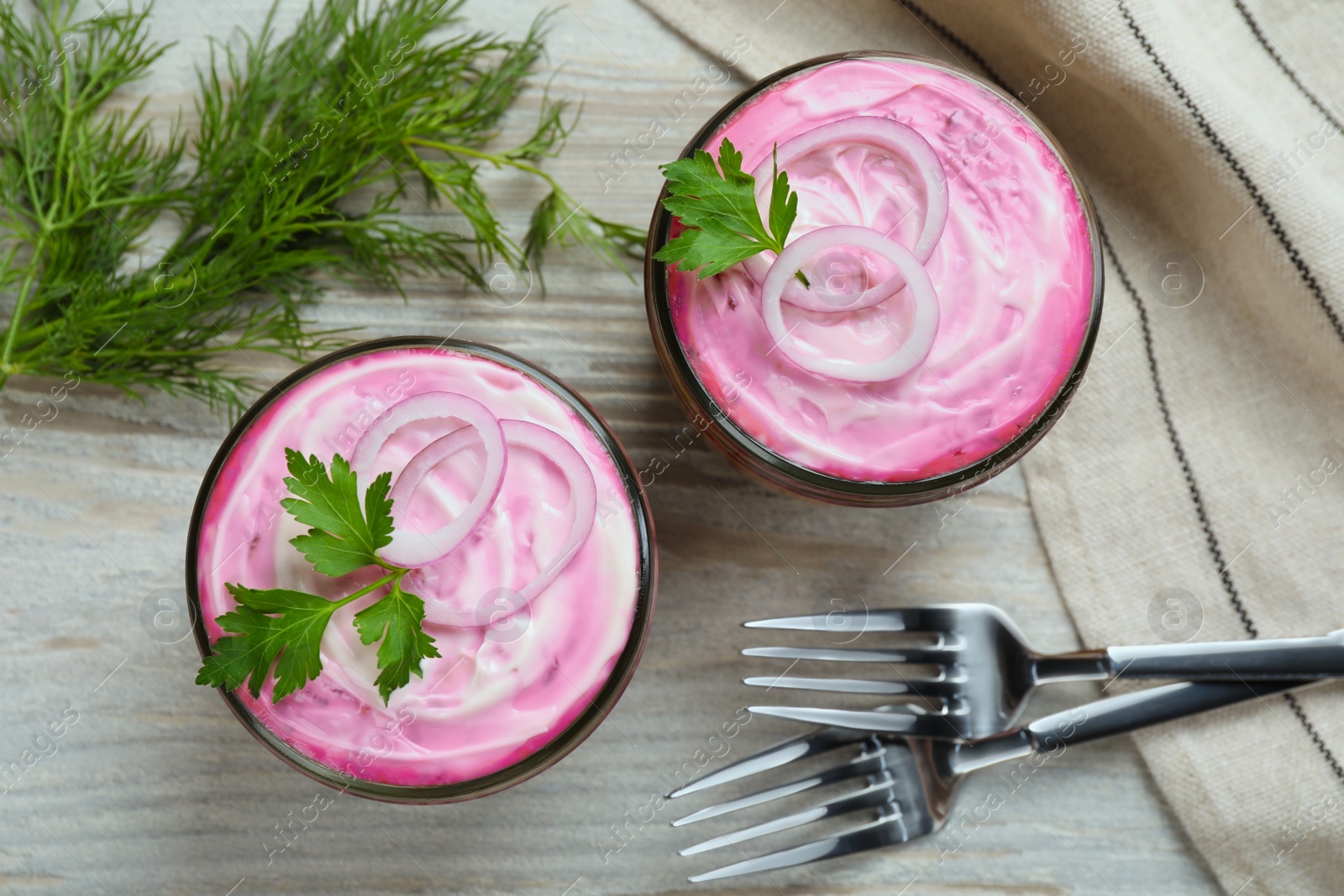 Photo of Glass jars of herring under fur coat on wooden table, flat lay. Traditional Russian salad