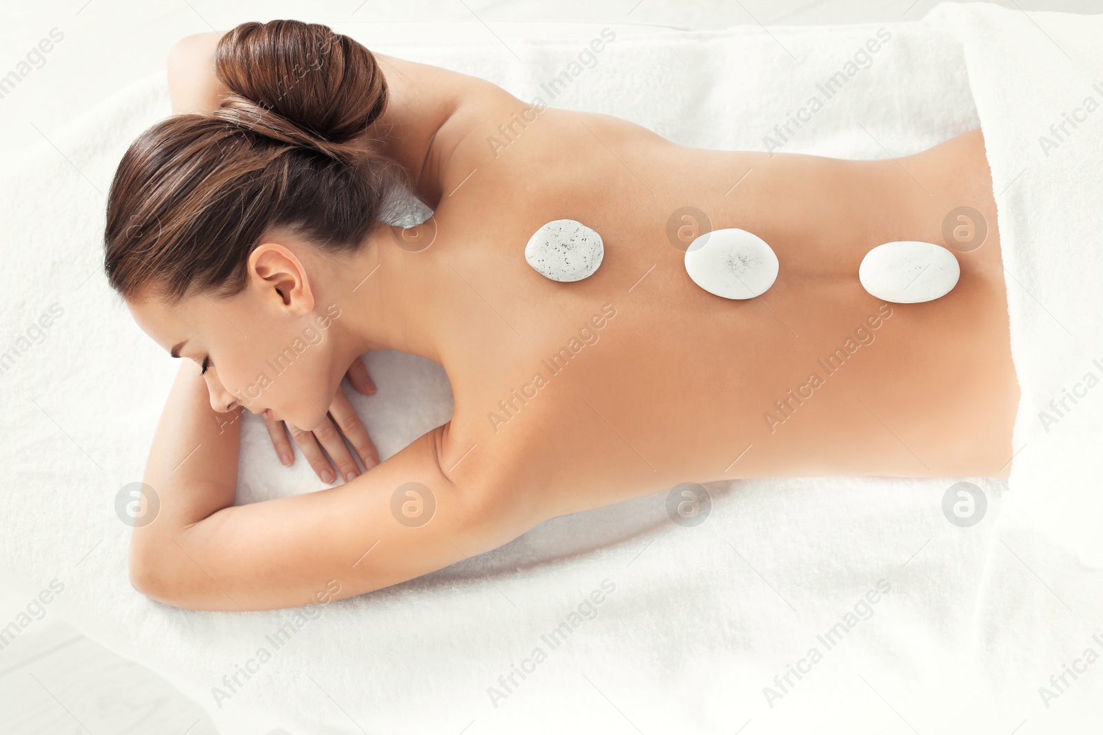 Photo of Young woman with stones on her back in spa salon