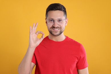 Portrait of happy man in stylish glasses showing ok gesture on yellow background