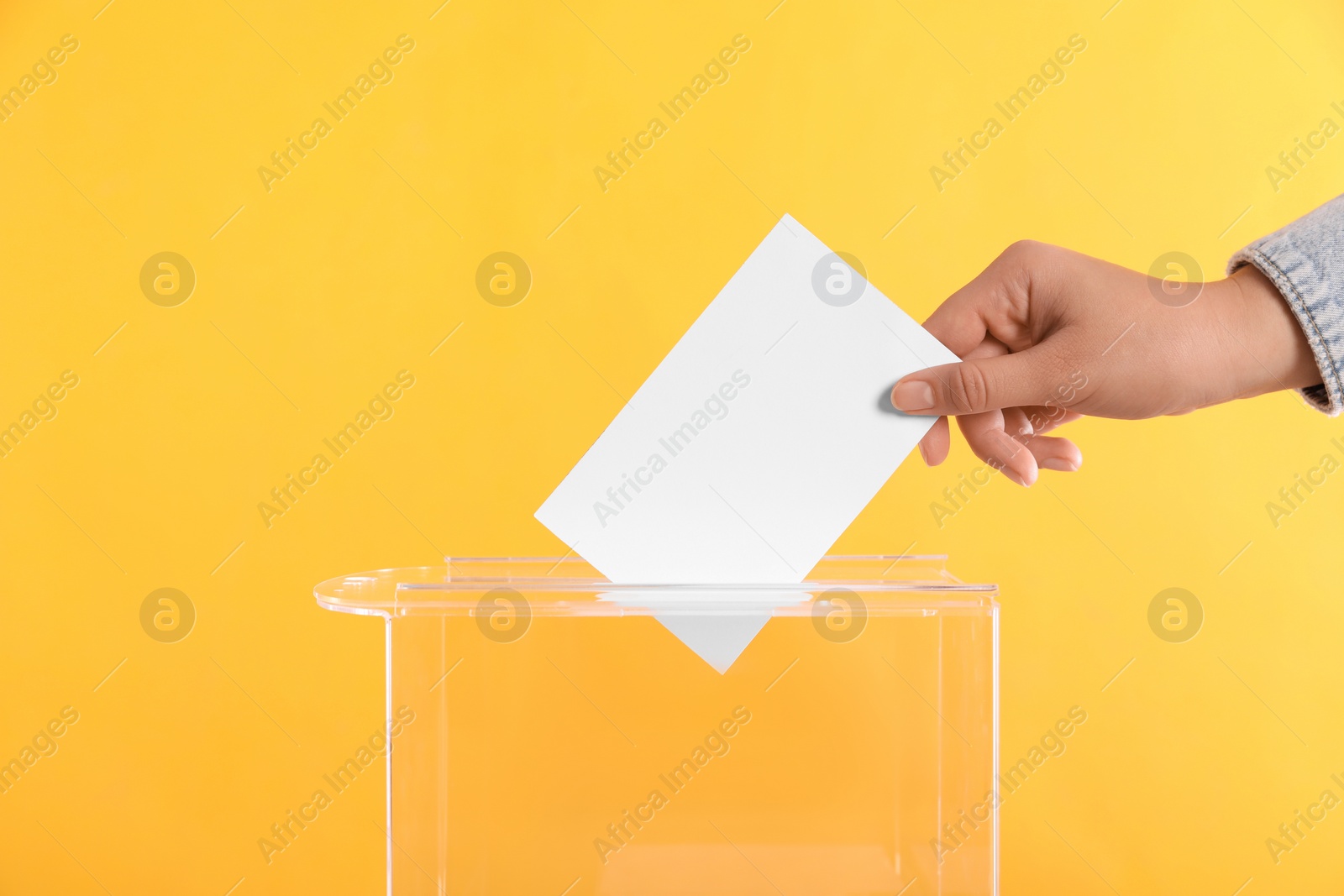 Photo of Woman putting her vote into ballot box on orange background, closeup