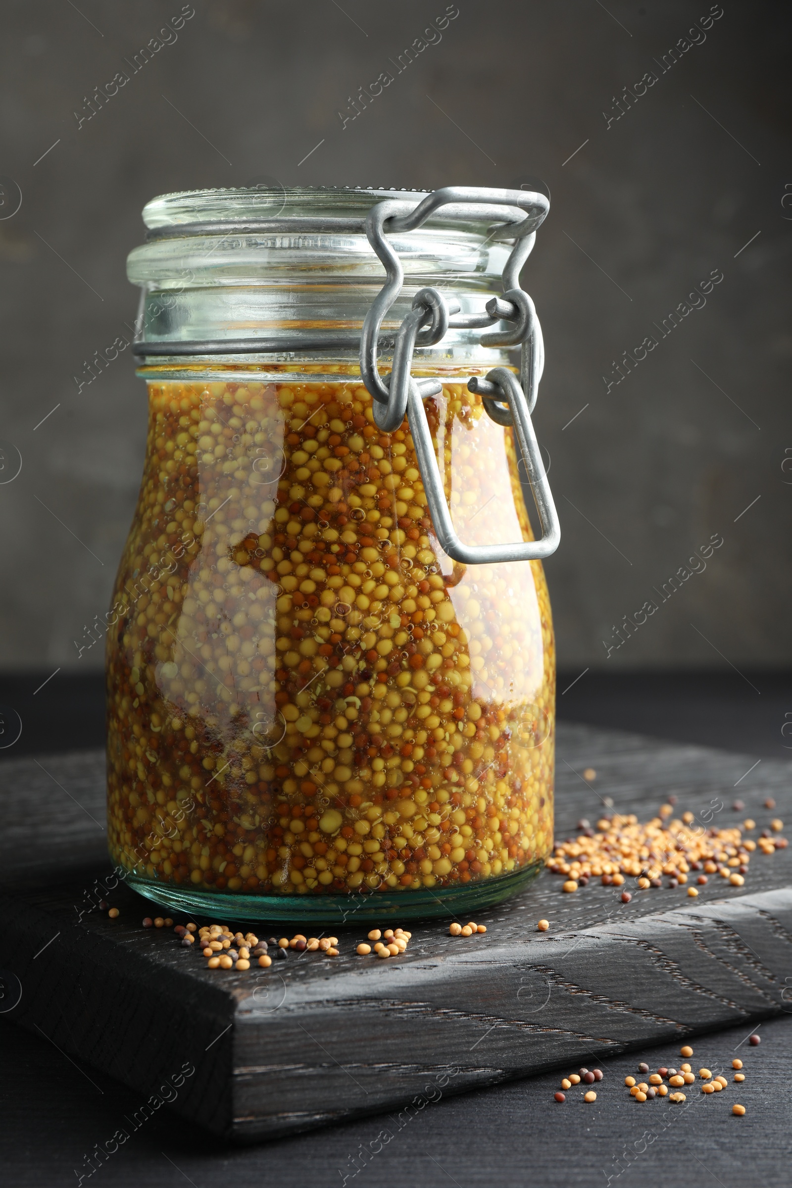 Photo of Whole grain mustard in jar and dry seeds on black table