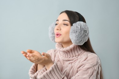 Beautiful young woman wearing earmuffs on light grey background