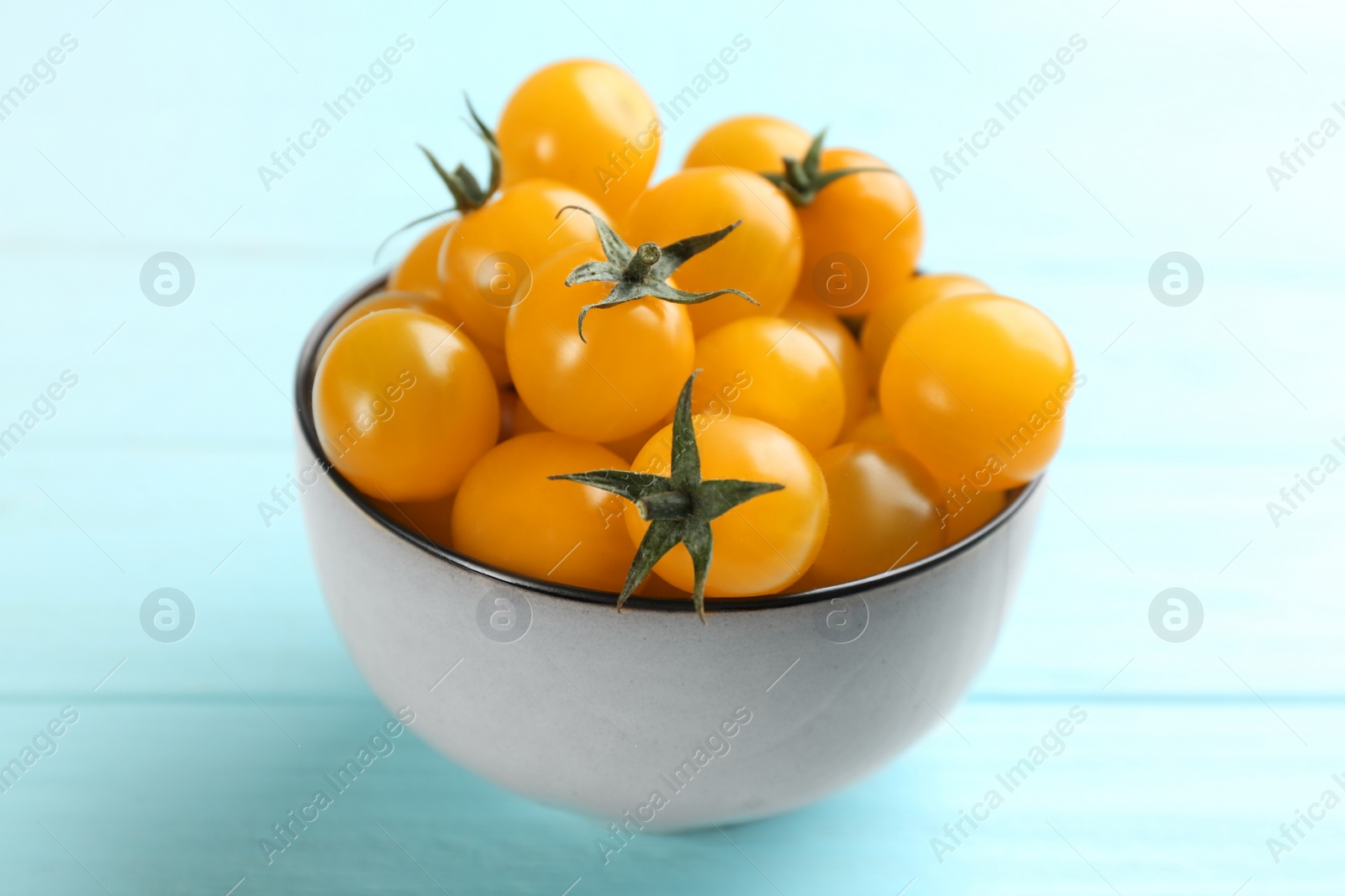 Photo of Ripe yellow tomatoes in bowl on light blue table