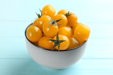 Photo of Ripe yellow tomatoes in bowl on light blue table