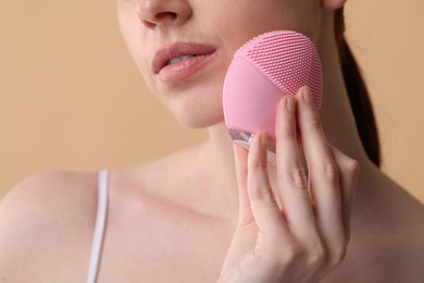 Washing face. Young woman with cleansing brush on beige background, closeup