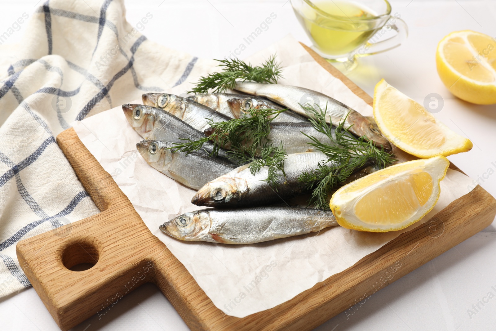 Photo of Fresh raw sprats, dill, oil and cut lemon on white table