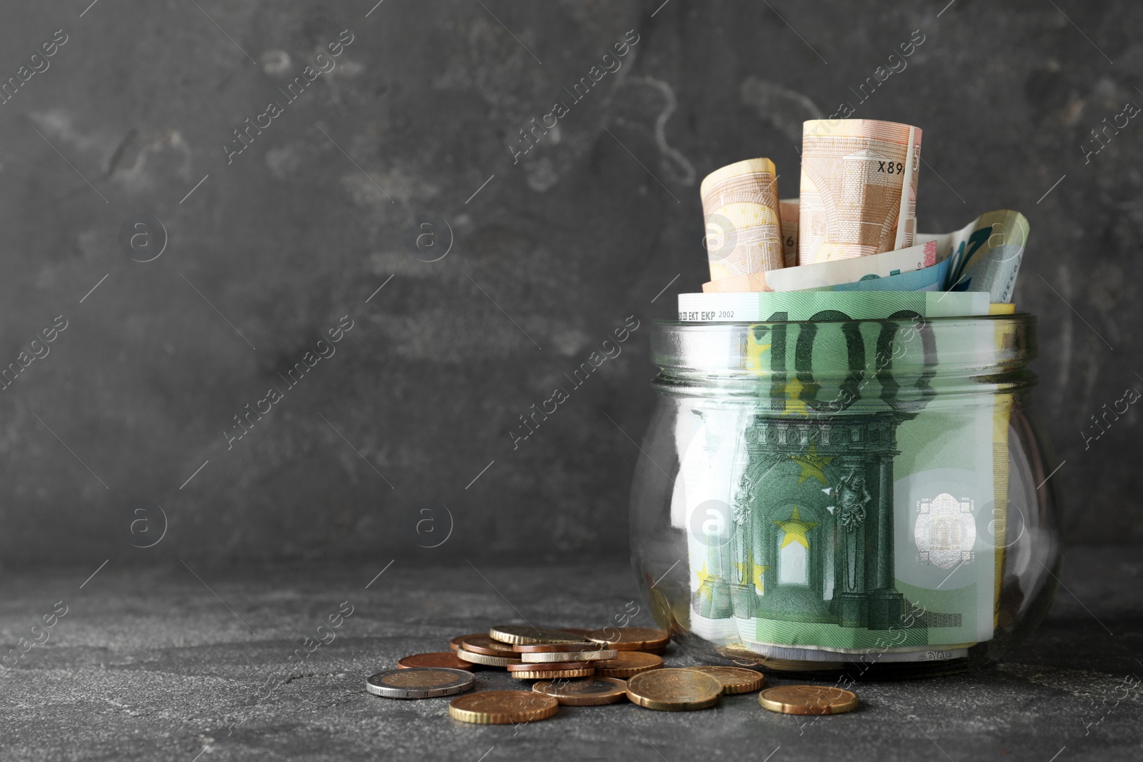 Image of Glass jar full of money on grey table. Space for text 