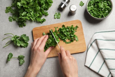 Photo of Woman cutting fresh green cilantro at light grey table, top view