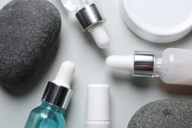 Photo of Bottles with cosmetic serum and stones on light grey background, flat lay