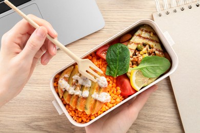 Woman eating healthy products high in vegetable fats near laptop at wooden table, top view