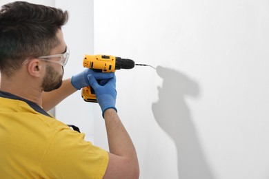 Young worker using electric drill indoors. Space for text