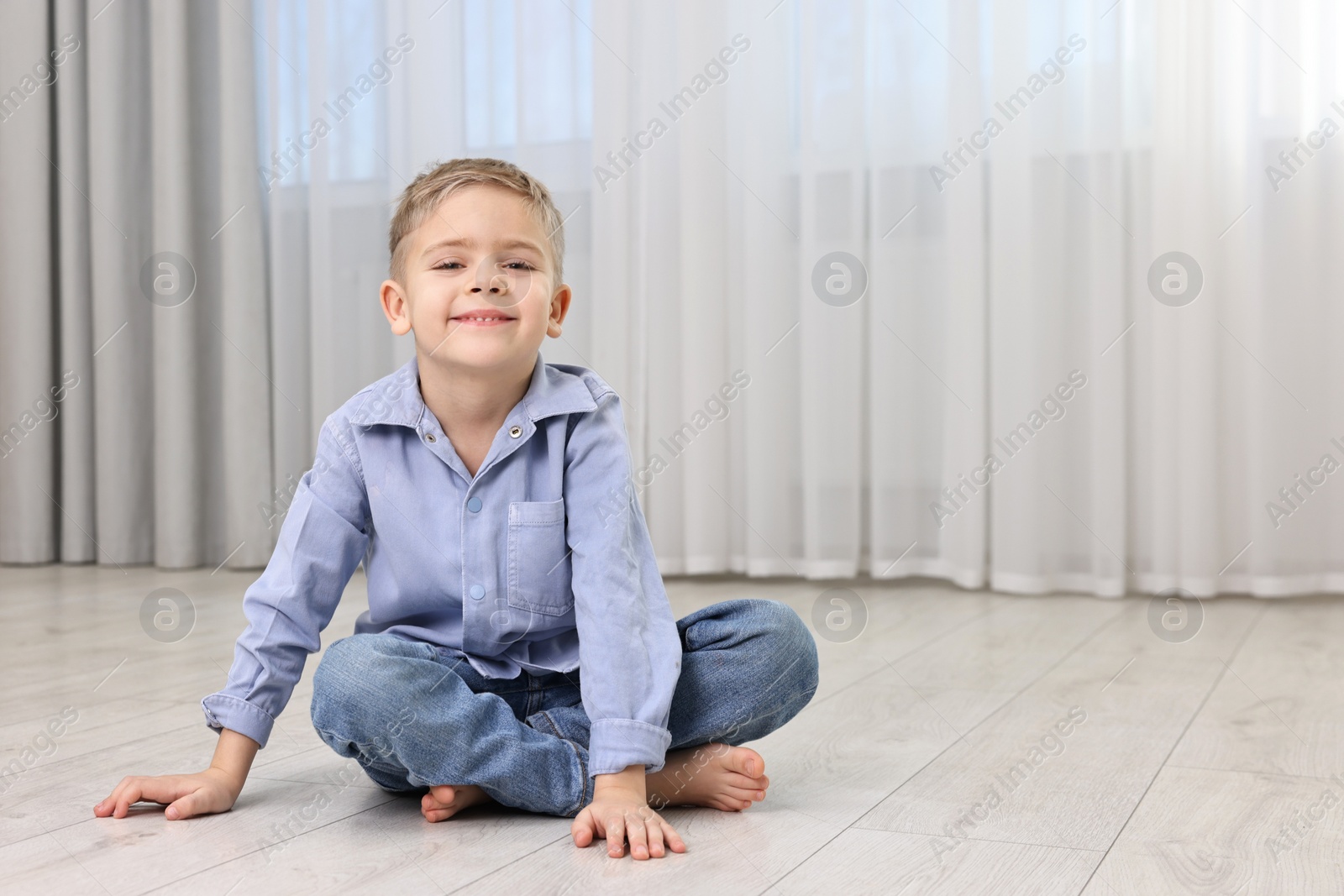 Photo of Cute little boy sitting on warm floor at home, space for text. Heating system