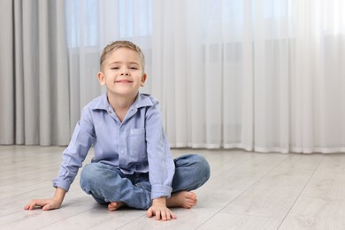 Cute little boy sitting on warm floor at home, space for text. Heating system