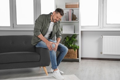 Photo of Man suffering from knee pain on sofa at home, space for text