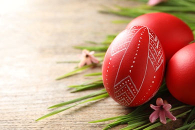 Photo of Red painted Easter eggs and green grass on wooden table, closeup. Space for text
