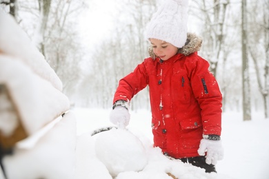 Photo of Cute little girl rolling snowball on bench in winter