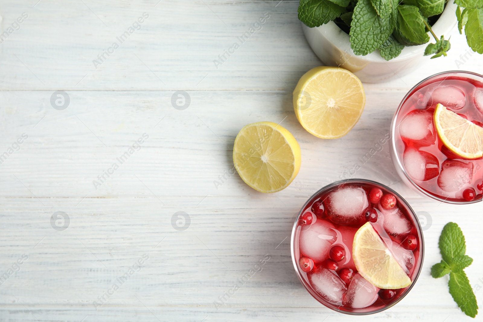 Photo of Tasty refreshing cranberry cocktails with lemon on white wooden table, flat lay. Space for text