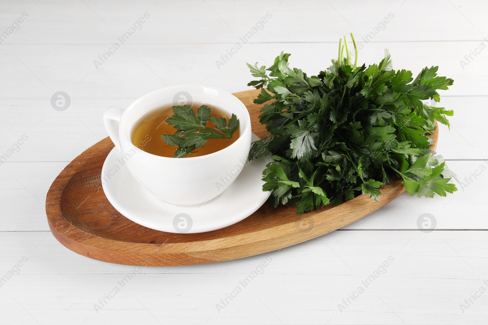 Photo of Aromatic herbal tea and fresh parsley on white wooden table