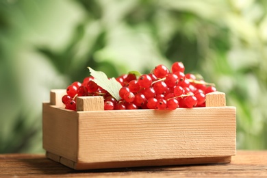 Photo of Ripe red currants in wooden crate on table against blurred background