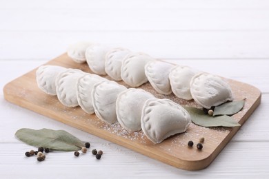 Photo of Raw dumplings (varenyky), peppercorns and bay leaves on white wooden table