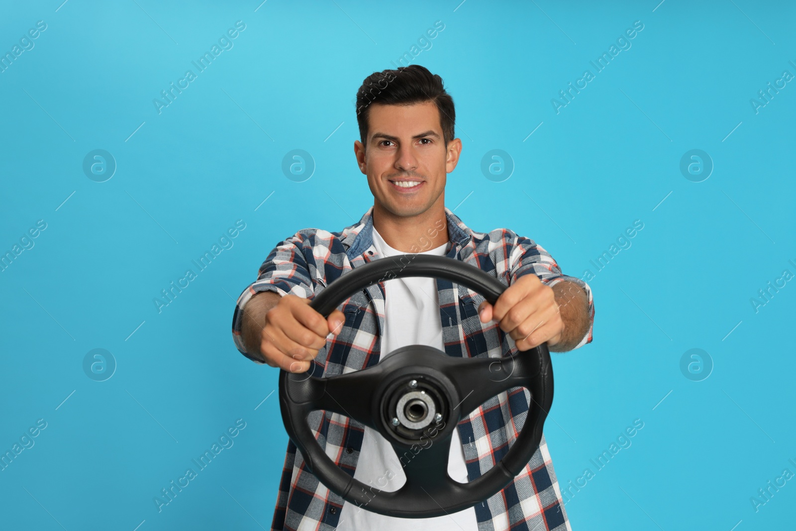 Photo of Happy man with steering wheel on light blue background. Space for text