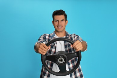 Photo of Happy man with steering wheel on light blue background. Space for text