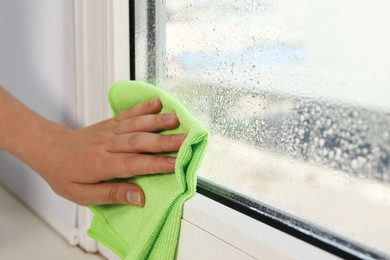 Photo of Woman wiping window glass with drops of condensate indoors, closeup