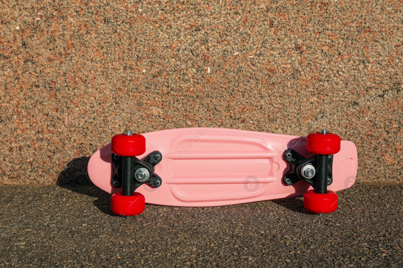Photo of Pink skateboard with red wheels on asphalt outdoors