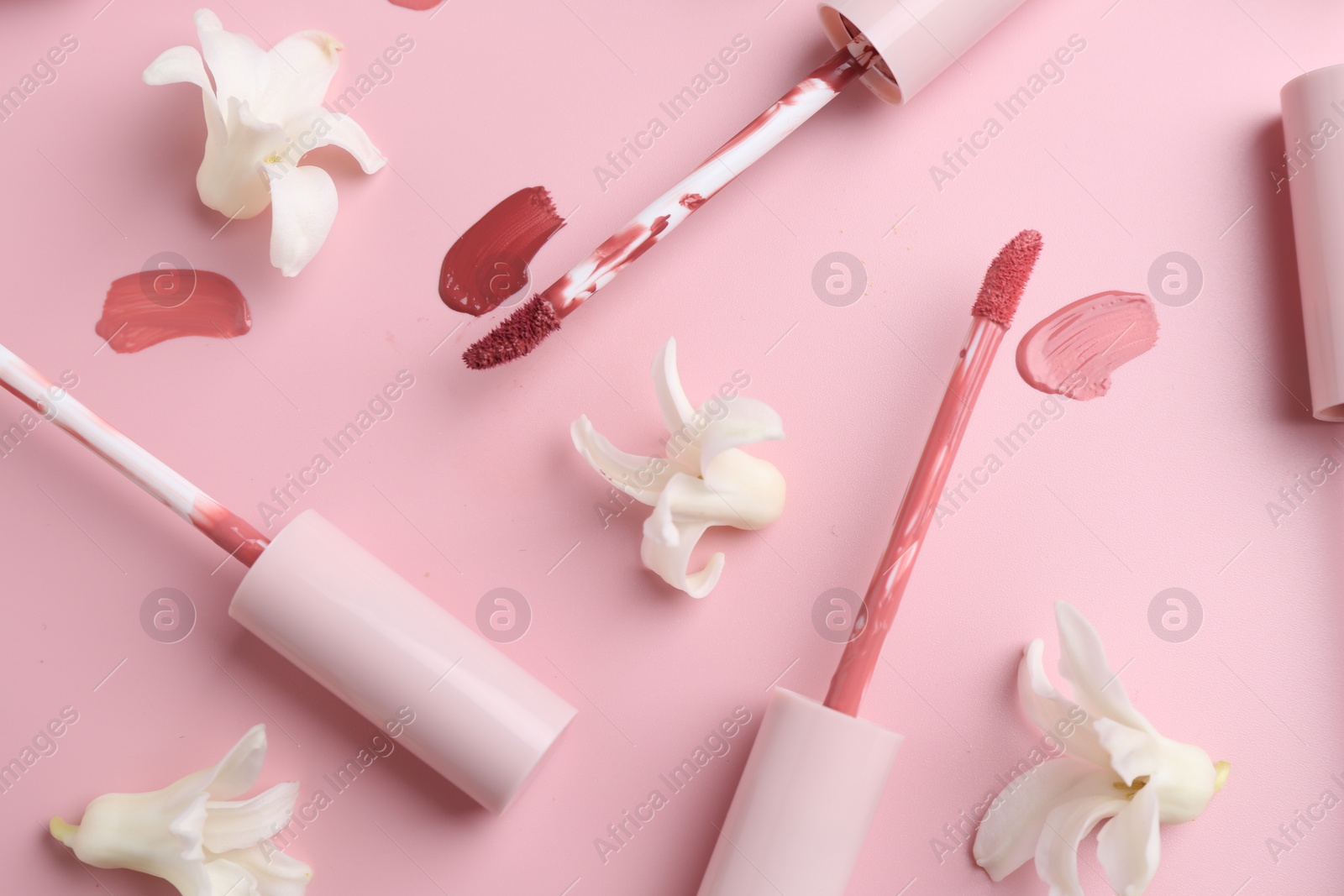 Photo of Different lip glosses, applicators and flowers on pink background, flat lay