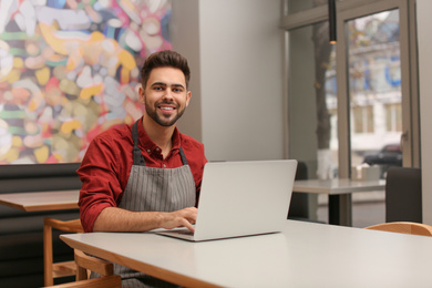 Young male business owner working with laptop in his cafe