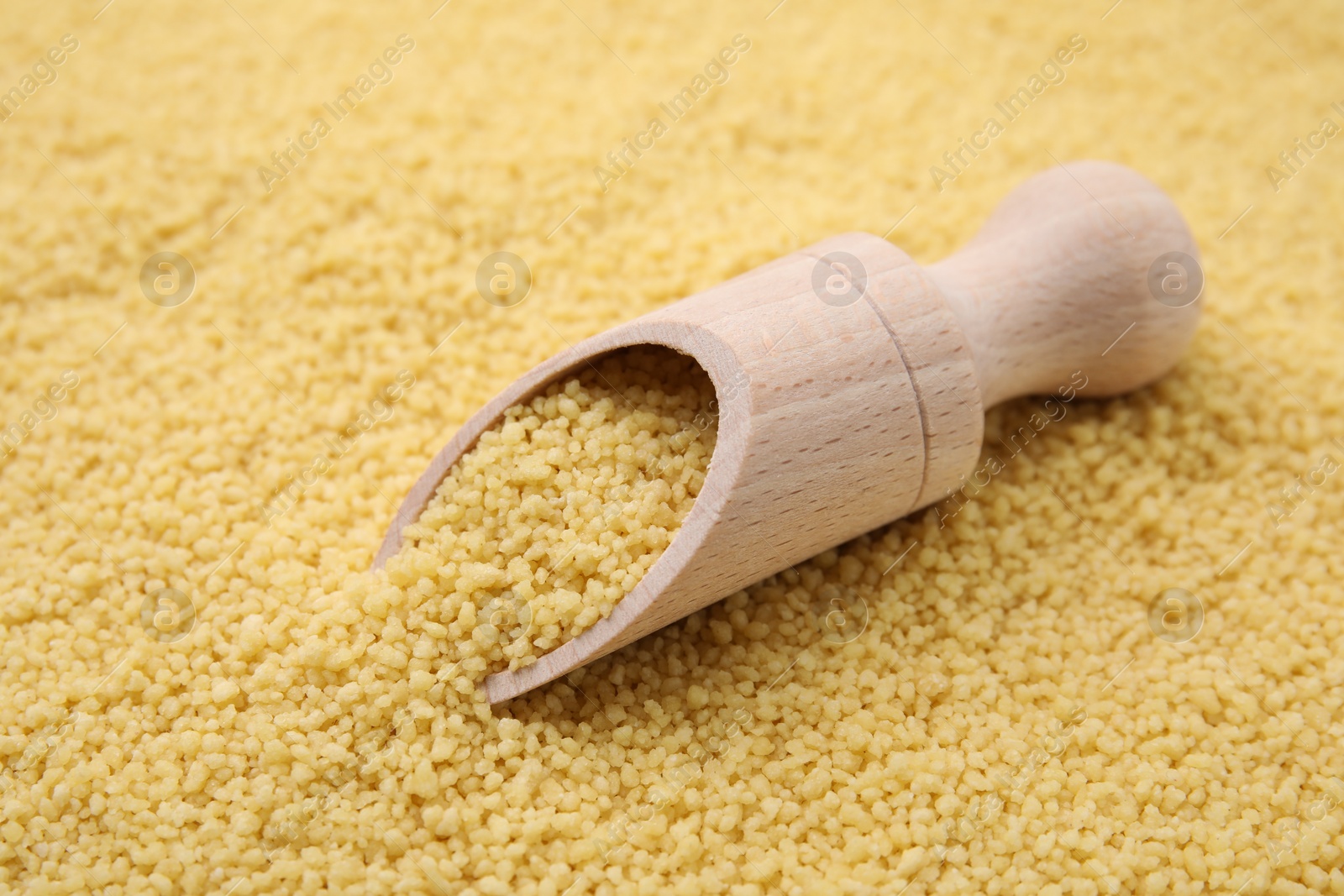 Photo of Wooden scoop and uncooked organic couscous as background, closeup