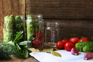 Photo of Glass jars, fresh vegetables and herbs on wooden table. Pickling recipe