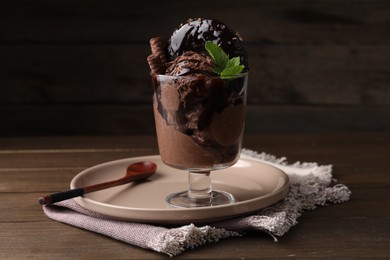 Photo of Delicious chocolate ice cream with wafer sticks, donut and mint in glass dessert bowl on wooden table