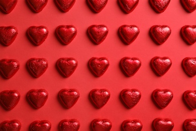 Tasty chocolate heart shaped candies on red background, flat lay