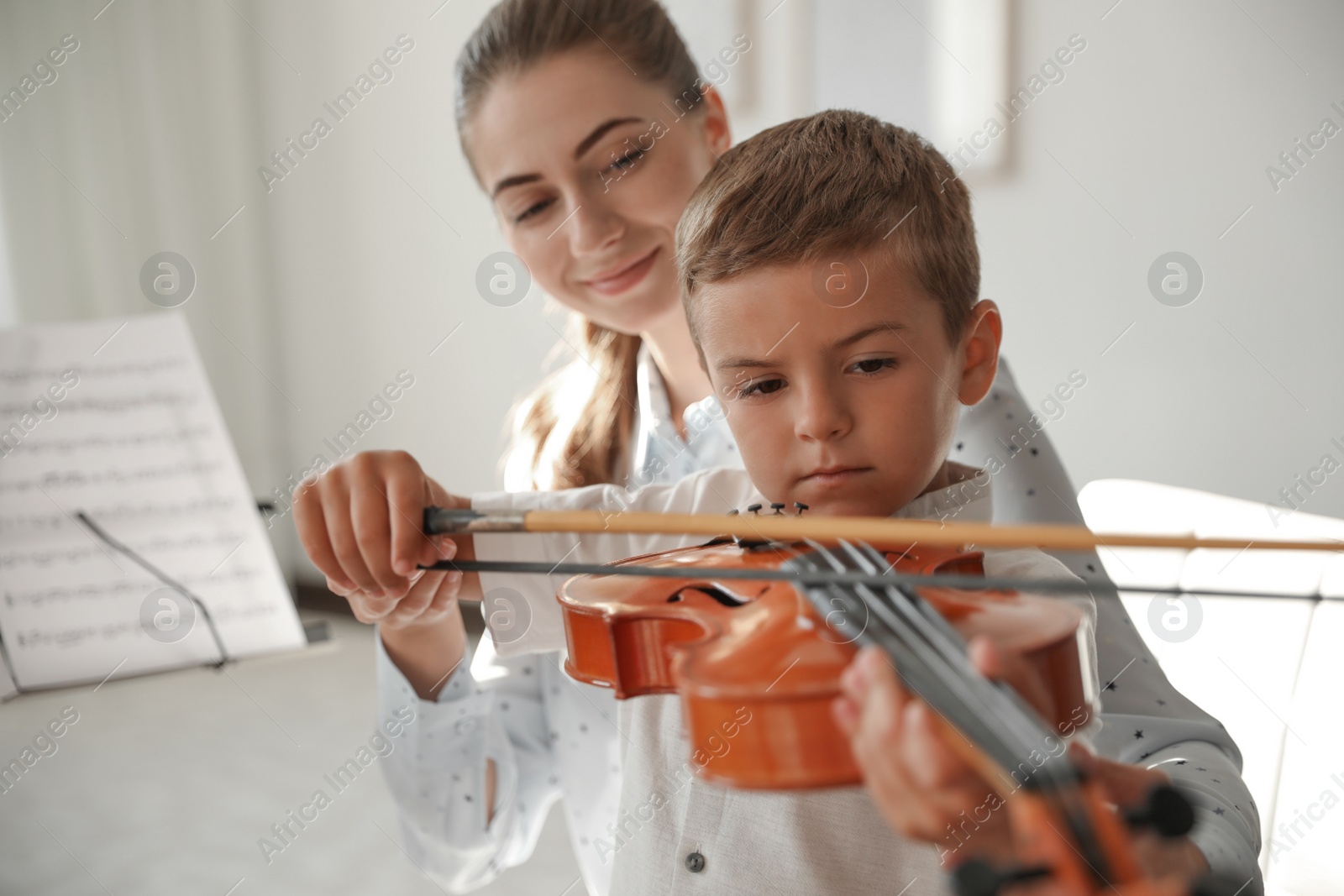 Photo of Young woman teaching little boy to play violin indoors