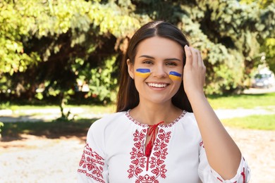 Photo of Young woman with drawings of Ukrainian flag on face in park